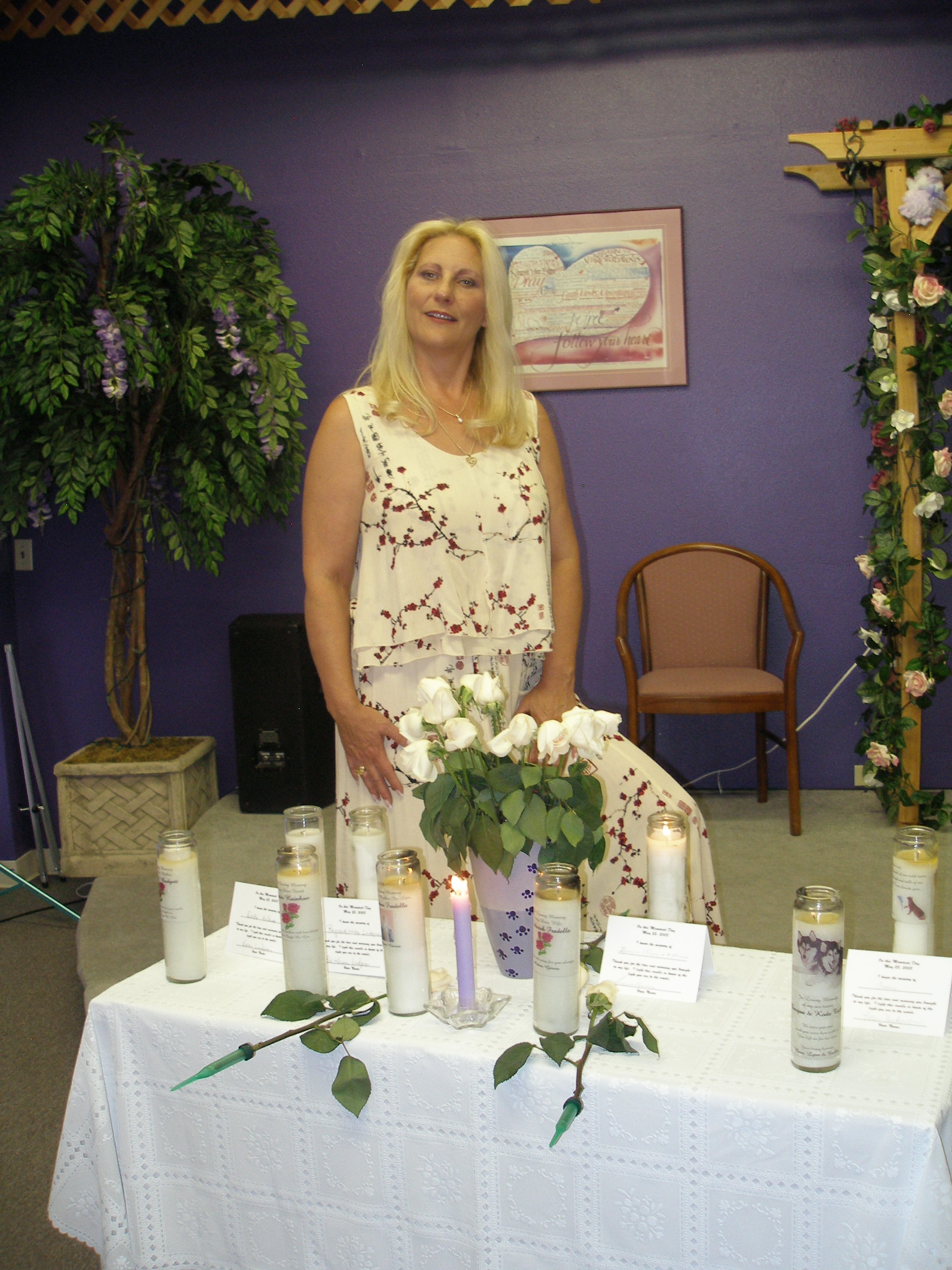 Woman standing at memorial candle display with white roses at Oasis CSL