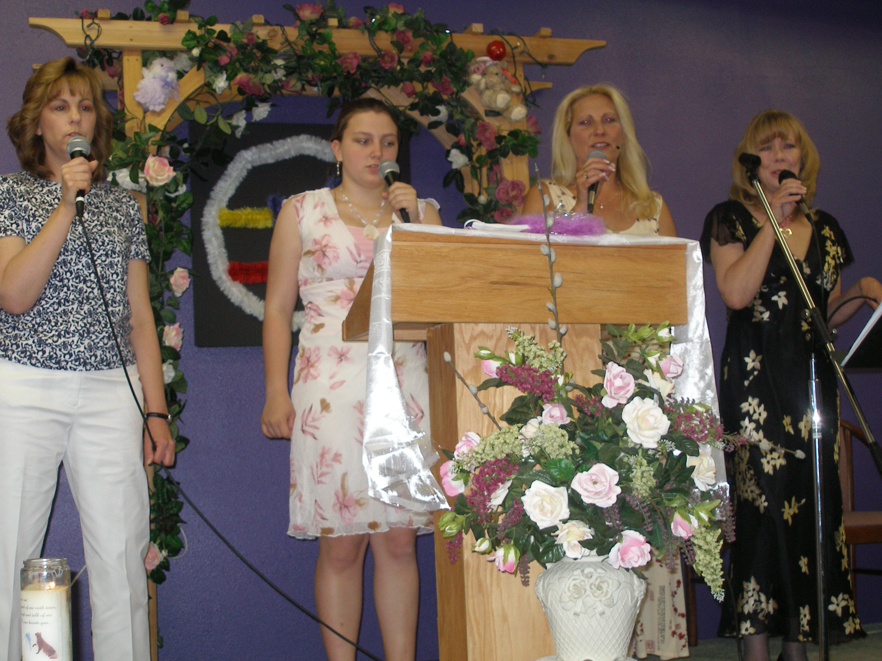 Four women singing at microphones on the Oasis CSL stage