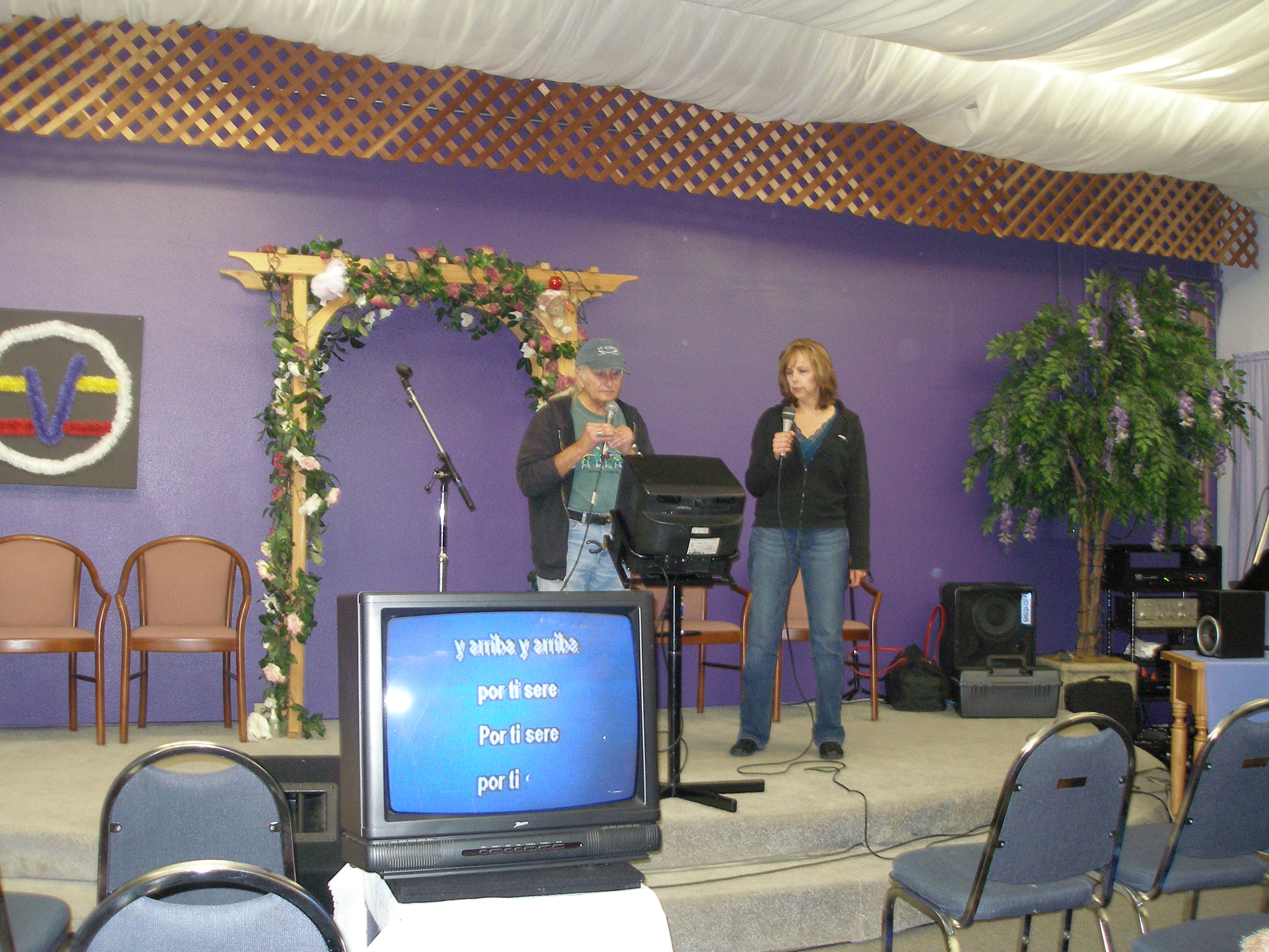 Two people singing on the Oasis CSL stage with floral arch and karaoke screen
