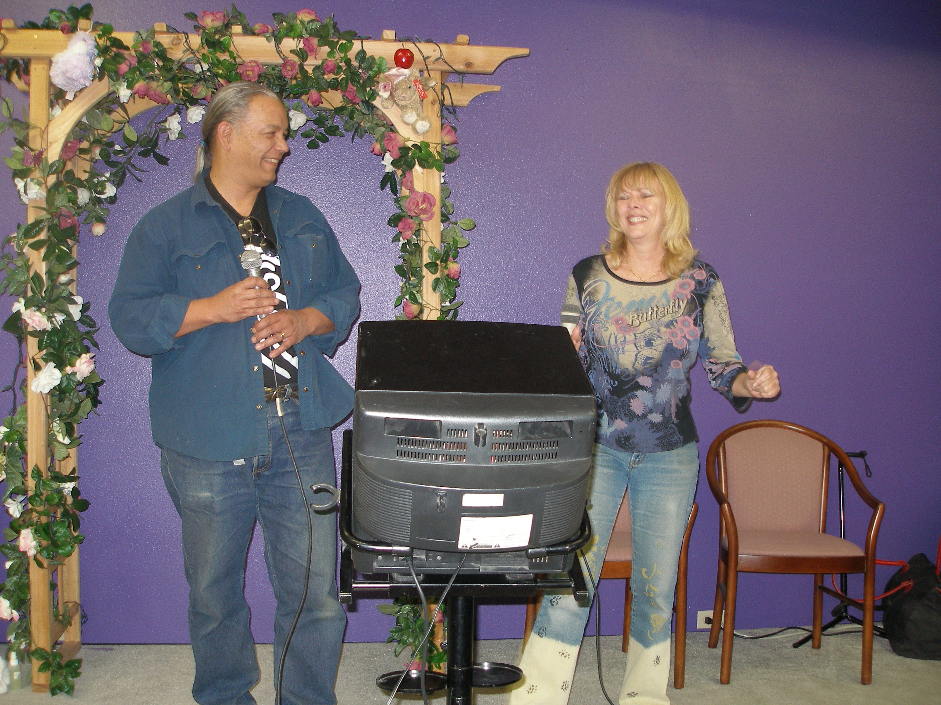 Man and woman laughing together by the floral arch at Oasis CSL karaoke event
