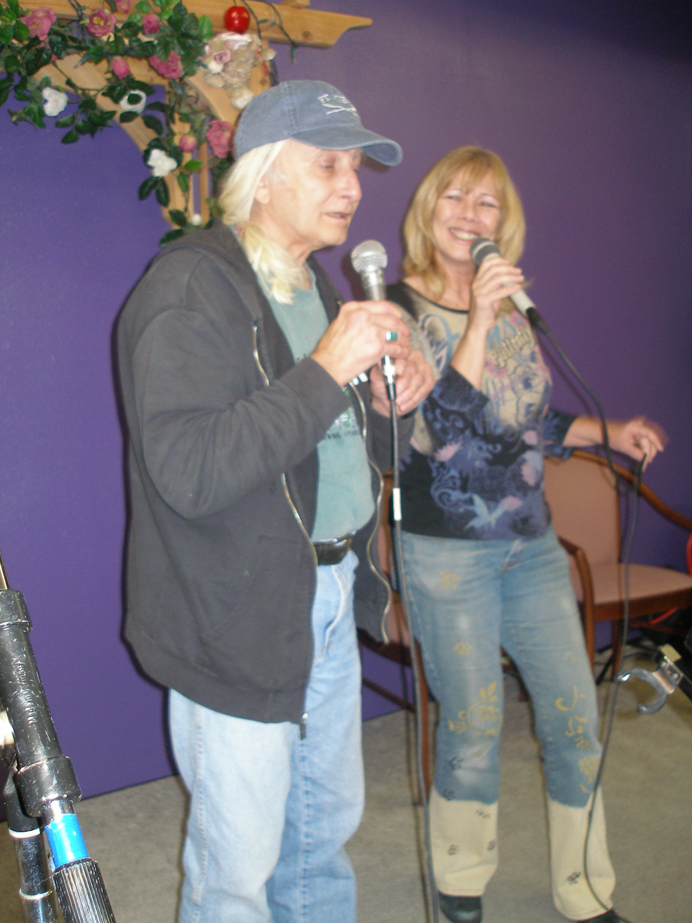 Two people singing together with microphones at Oasis CSL purple wall event
