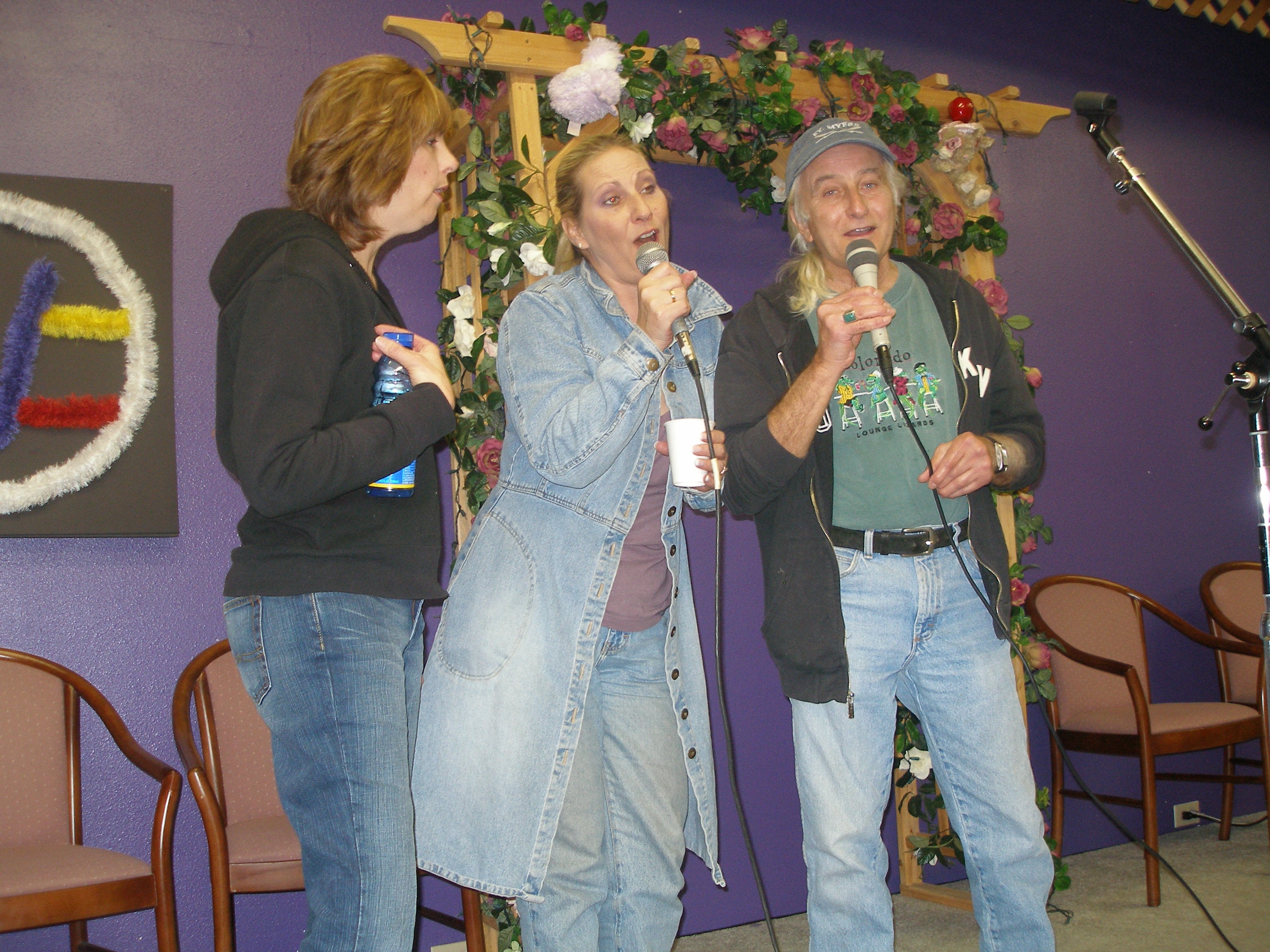 Three people singing together at Oasis CSL community event with floral arch