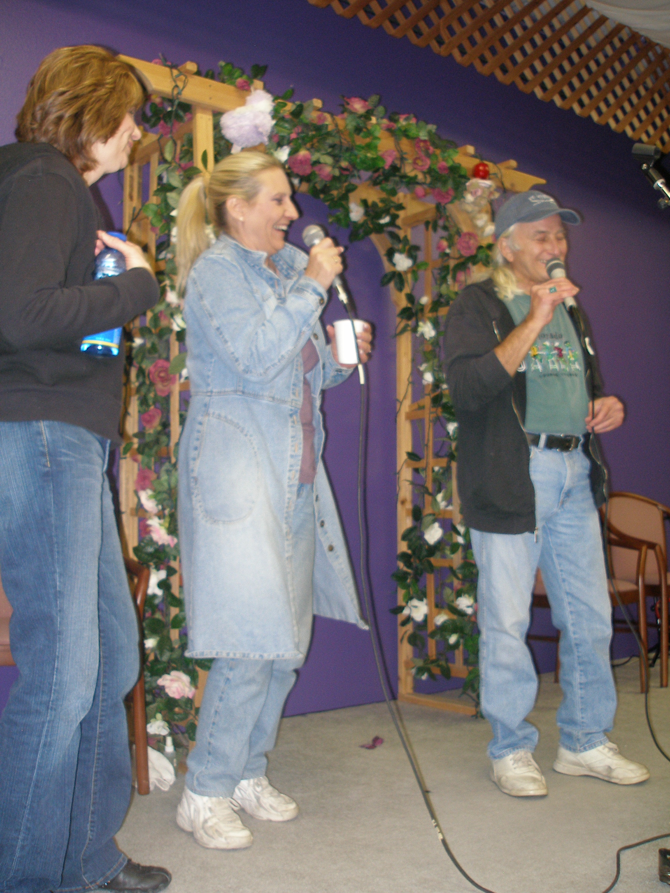 Three people performing together at Oasis CSL event with floral arch backdrop