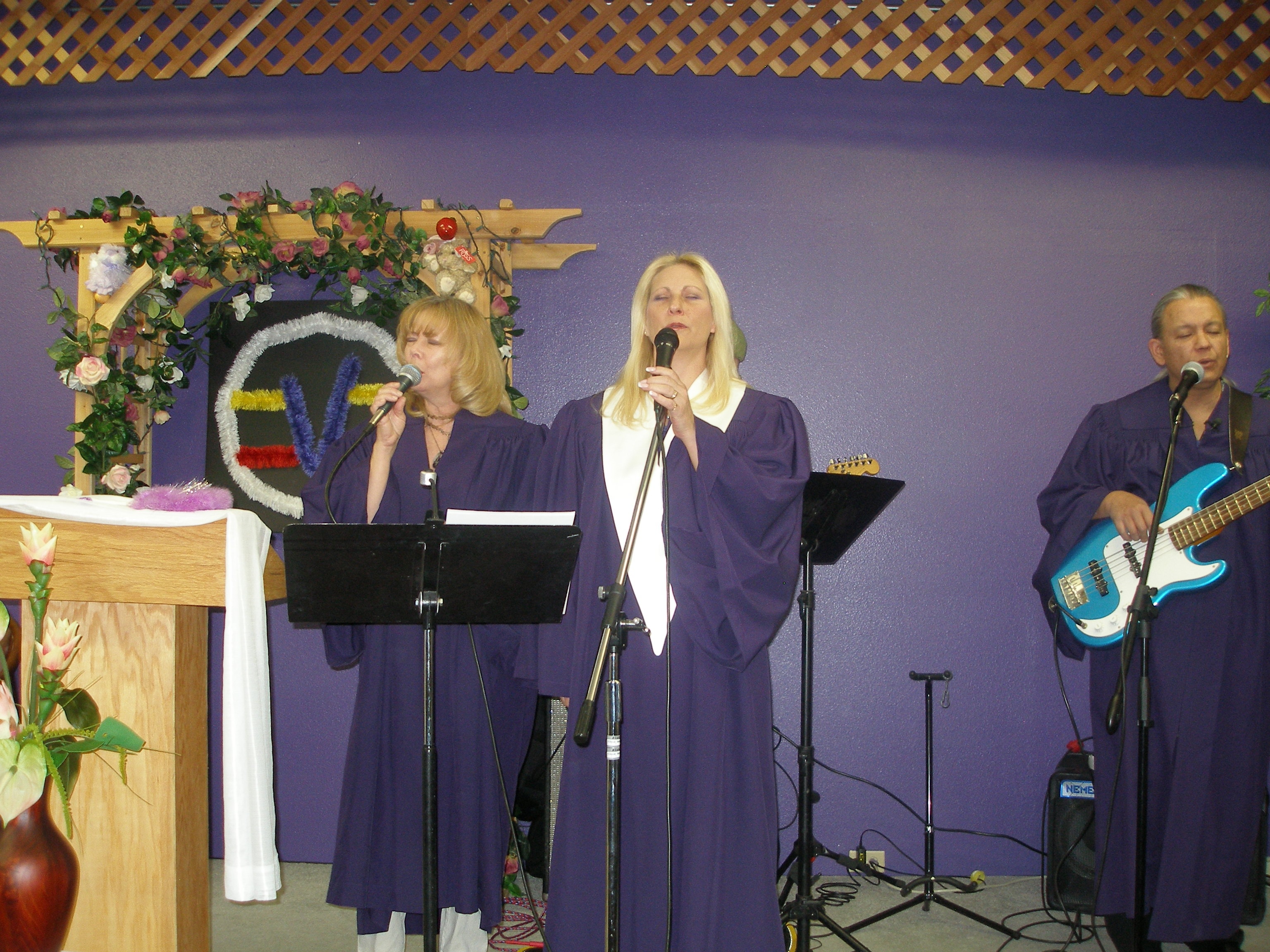Three robed performers singing on stage at Rev. S. Tucker's ordination