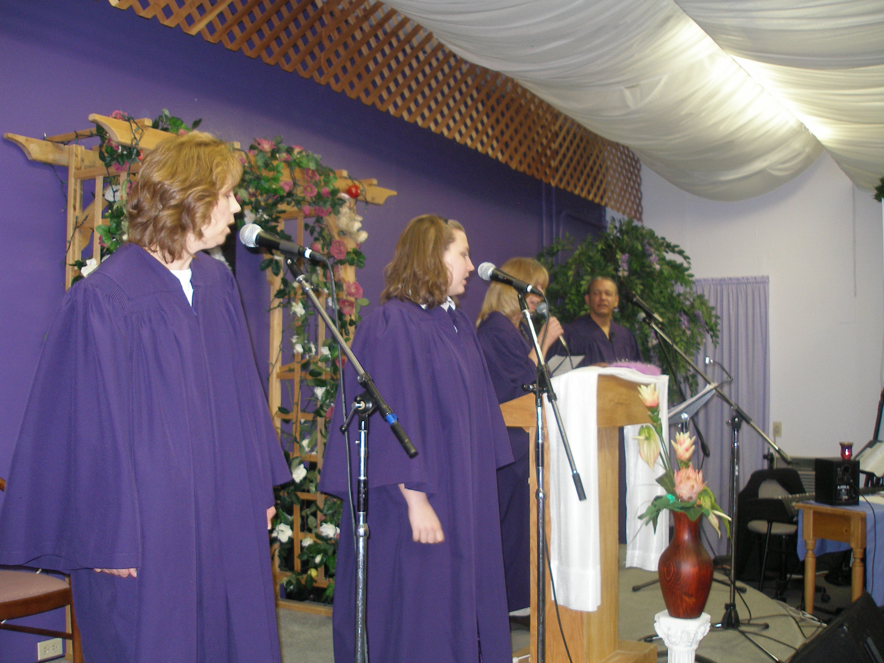 Two women in purple robes singing at microphones at Rev. S. Tucker's ordination